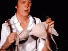 a man in a white shirt and suspenders is holding a bra and a microphone .