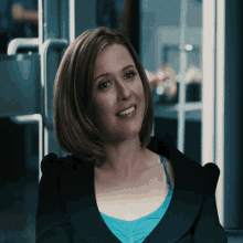 a woman wearing a blue tank top and a black jacket smiles for the camera