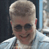 a woman wearing glasses and a denim jacket smiles for the camera