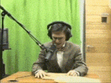 a man wearing headphones is reading a book in front of a green curtain