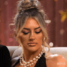 a woman wearing a pearl necklace is sitting on a couch next to a man