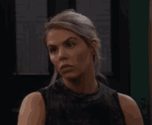 a woman in a black tank top is looking at the camera and making a funny face .
