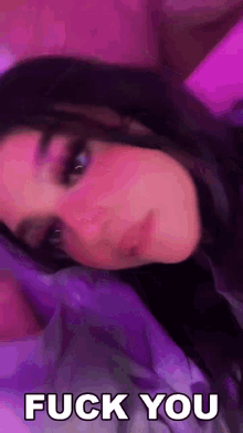 a woman is laying on a bed with a purple blanket and the words `` fuck you '' on her face .
