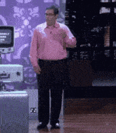 a man in a pink shirt and black pants stands in front of a screen that says terribly sad