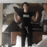 a man wearing a black shirt that says hood is standing on a bed
