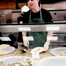 a man in a green apron is standing behind a counter with plates of food and a sign that says pizza sauce