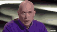 a bald man in a purple sweater is making a funny face while talking on a television show .
