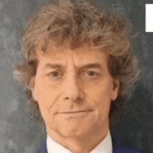 a man with curly hair is wearing a suit and tie and making a face .