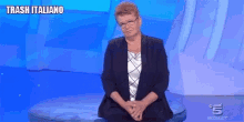 a woman wearing glasses and a black jacket is sitting on a blue couch on a television show .