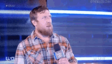 a man in a plaid shirt is holding a microphone and talking into it .