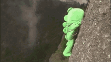 a green stuffed animal is climbing a rock wall .