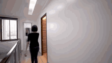 a woman in a black shirt is walking down a hallway towards a door