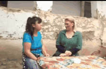 two women are sitting at a table talking to each other and smiling .