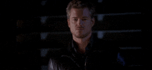 a man with a beard is wearing a black leather jacket and standing in the dark .