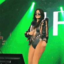 a woman wearing sunglasses and a swimsuit is singing into a microphone on a stage with a letter h in the background