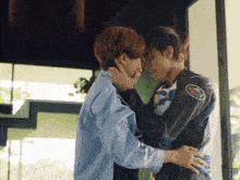a man in a motorcycle jacket is hugging another man in a shirt .