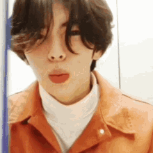 a young man with long hair is wearing an orange jacket and a white turtleneck and making a funny face .