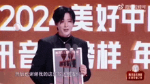 a man is standing in front of a microphone holding a magazine in front of a sign that says `` 2021 '' .