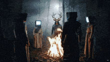 a group of people with television heads standing around a fire
