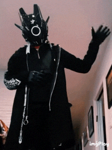 a person in a black costume is standing in a hallway waving .