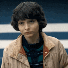a close up of a young boy wearing a jacket and a striped shirt