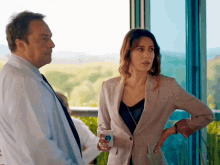 a man and a woman are standing next to each other in front of a large window