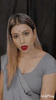 a woman with red lipstick and a bindi on her forehead looks at the camera with imgplay in the corner