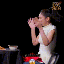 a woman is sitting at a table with her hands in the air and a bowl of food .
