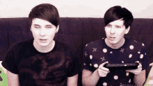 two young men are sitting next to each other on a couch and one is holding a video game controller .