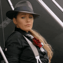 a woman wearing a fedora hat and suspenders looks at the camera