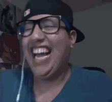 a man wearing glasses and a blue headband is laughing with his mouth wide open .