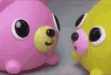 two stuffed animals , a pink and a yellow , are looking at each other .