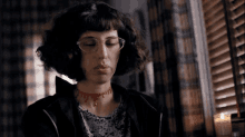 a woman wearing glasses and a choker with the letter t on it looks down