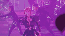 a woman is singing into a microphone on a stage while a group of dancers perform behind her .