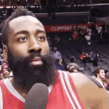 a man with a beard is talking into a microphone while wearing a red jersey .