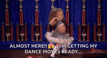 a little girl is dancing in front of trophies and says almost here