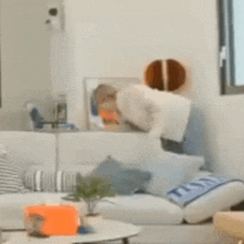 a person is standing on a couch in a living room with a basketball on the wall .