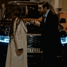 a man and a woman are standing in front of a black car with a license plate that says 4lt432
