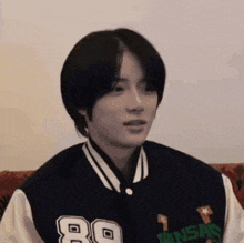 a young man is sitting on a couch wearing a baseball jacket with the number 80 on it .