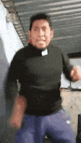 a man in a black shirt and blue pants is dancing in a garage .