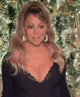 a woman with a very plunging neckline and earrings stands in front of a christmas tree