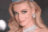 a woman wearing a tiara and a necklace smiles for the camera