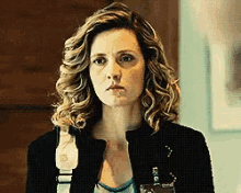 a woman with curly hair is wearing a black jacket and a name tag that says ' i ' on it .