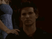a woman in a blue dress stands next to a man in a dark room