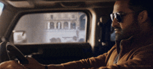 a man wearing sunglasses is driving a car with nandamurifans.com written on the bottom of the screen