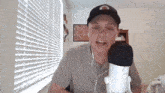 a man wearing a hat is talking into a microphone in front of a window