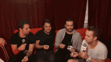 a group of men are sitting on a couch holding microphones and one of them is wearing a white shirt with the word nova on it