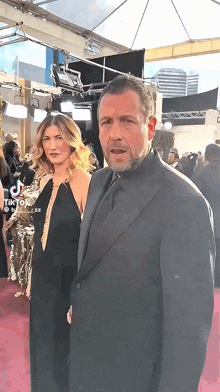 a man in a suit and tie stands next to a woman on a red carpet