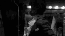 a black and white photo of a man in a tuxedo standing in a room .
