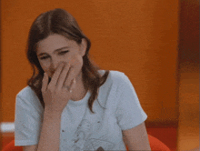 a woman covering her mouth with her hand while wearing a white t-shirt